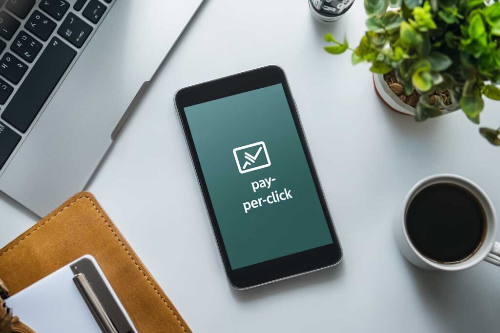 A smartphone displaying PPC concepts on a workspace with a coffee cup and laptop, representing digital ad strategies.