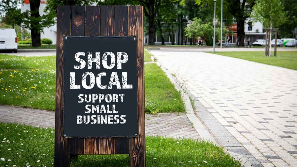 Wooden sidewalk sign reads _Shop Local Support Small Business.