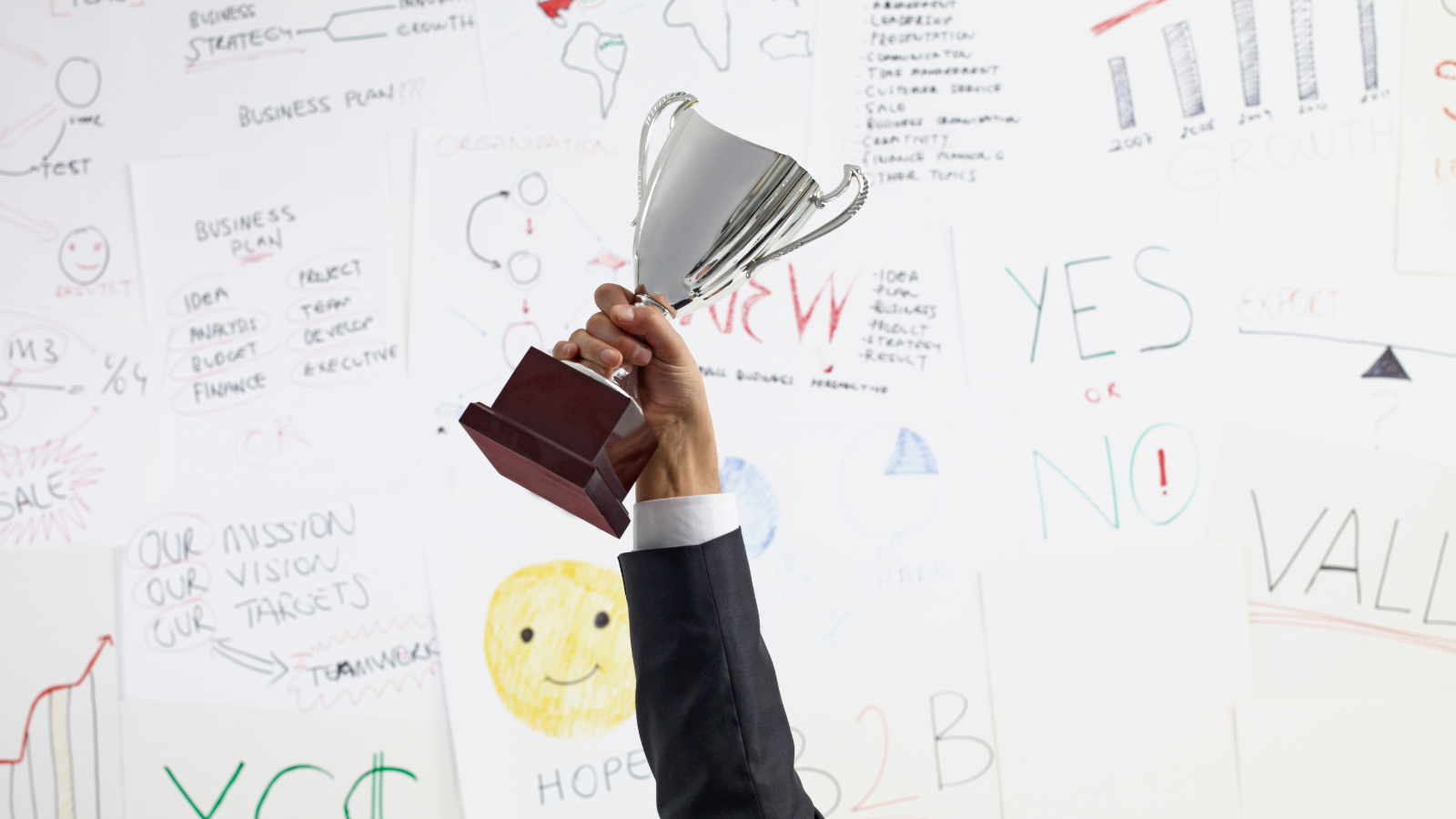 Hand holding up a trophy in front of business planning sketches