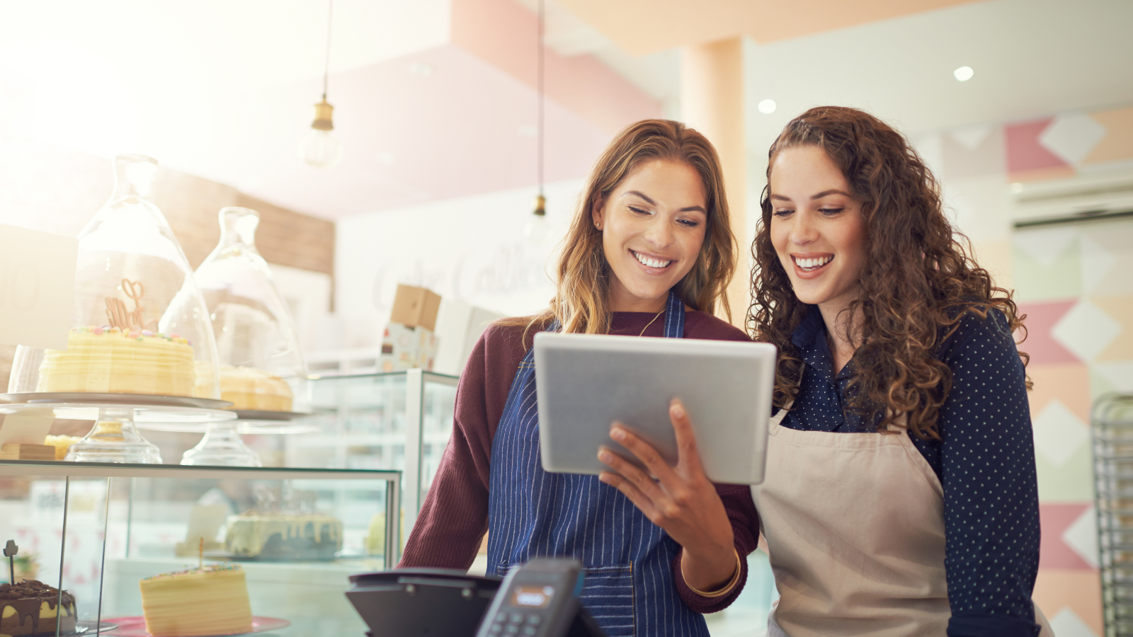 Two smiling women in a bakery looking at a tablet