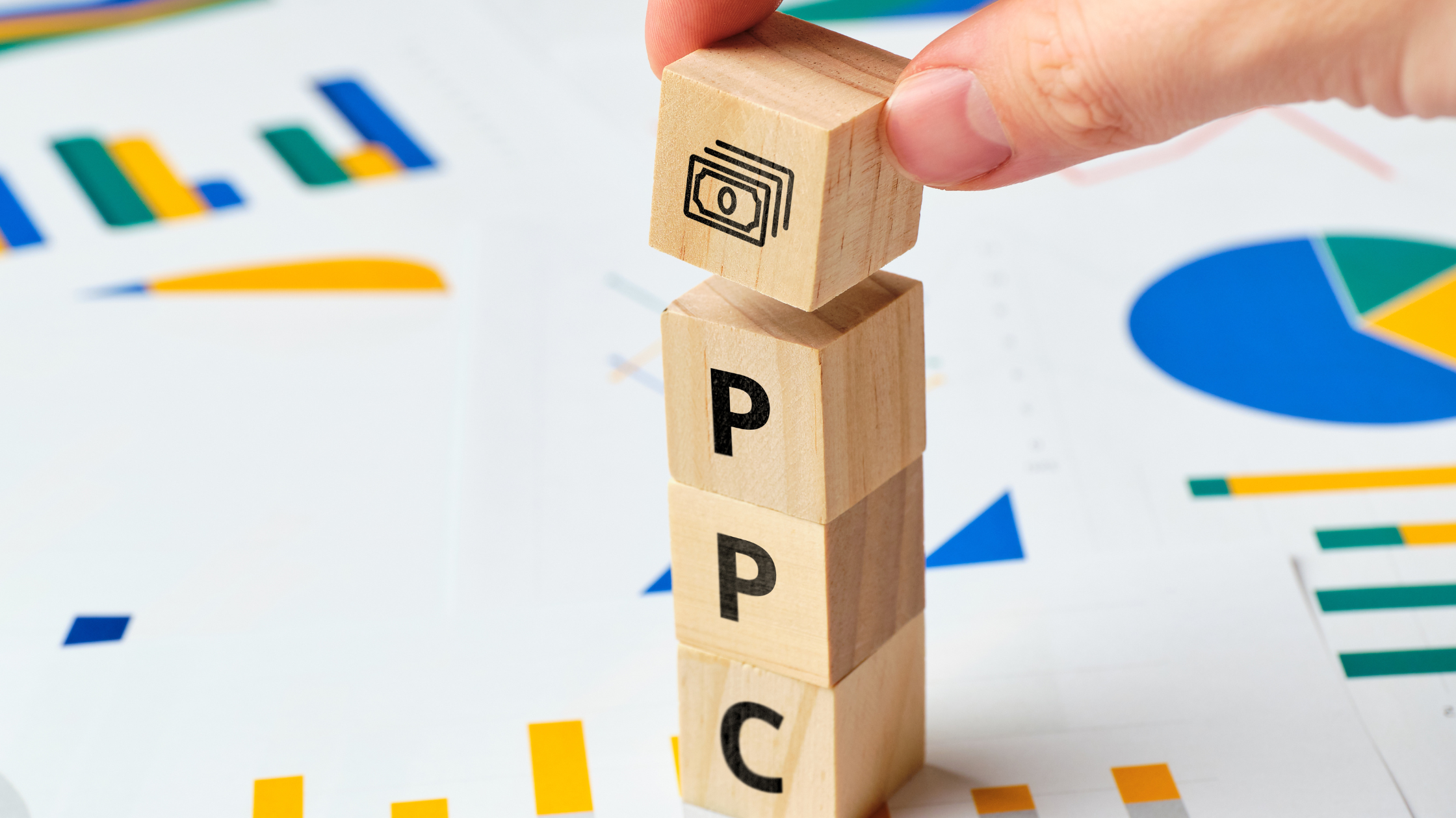 Wooden blocks spelling PPC placed on top of documents showing PPC statistics and charts