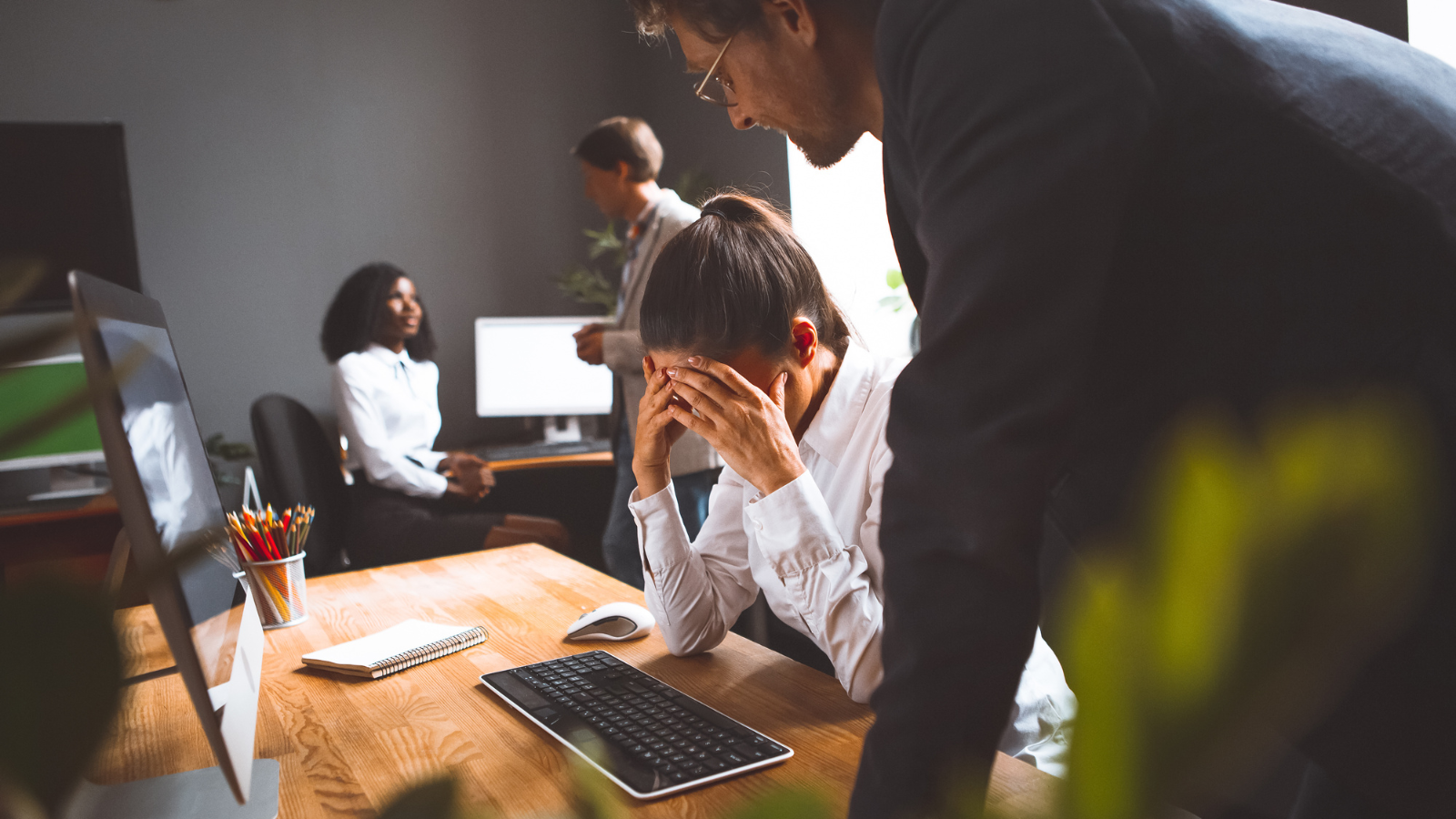  Stressed person at a desk while colleagues discuss in the background
