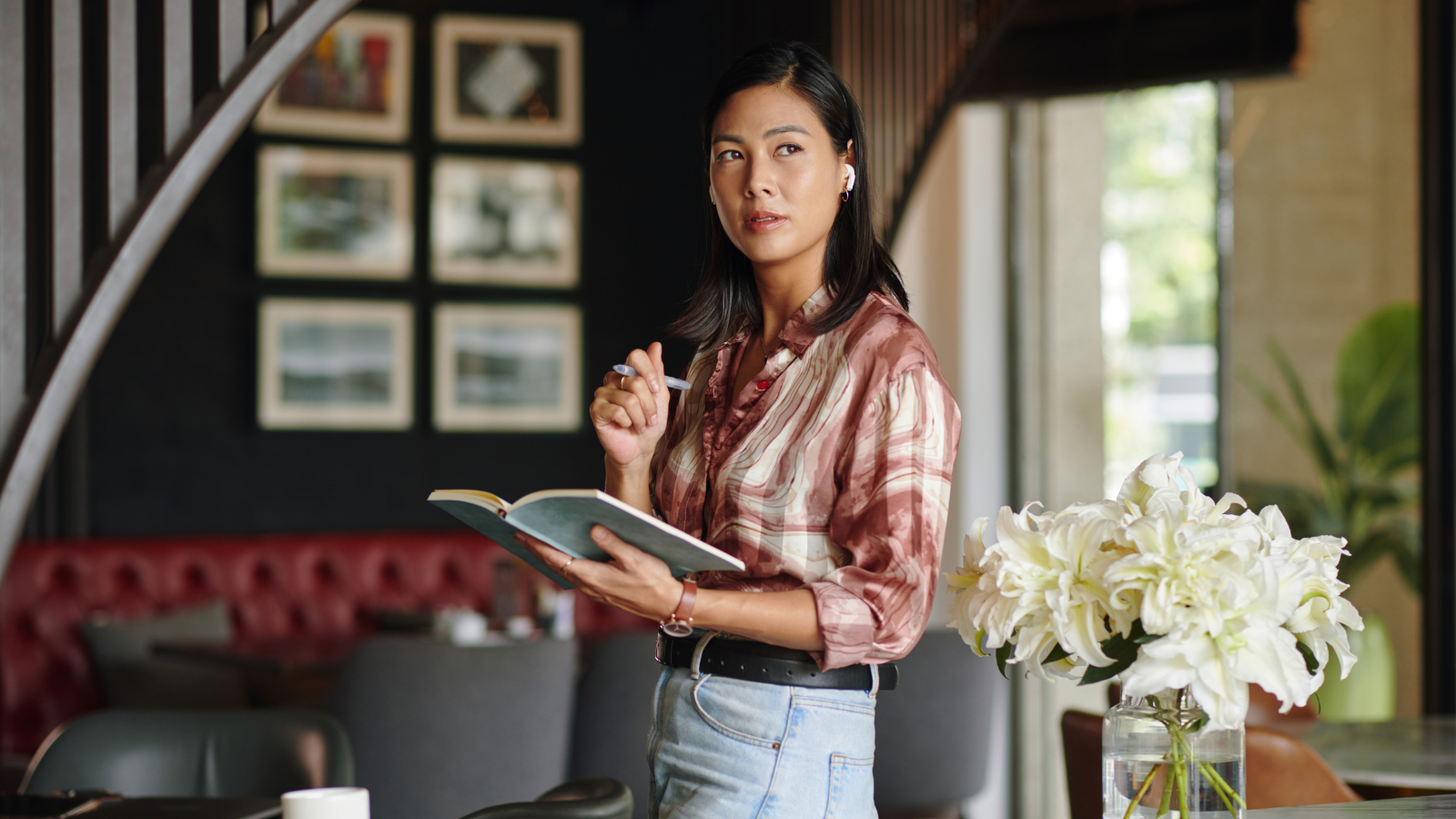 A woman holding a notebook and pen, standing in a cafe