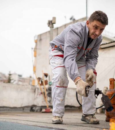 Worker-using-a-blowtorch-to-apply-a-waterproofing-membrane-on-a-rooftop-1536x864